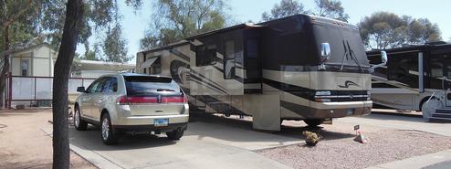 Wide exterior shot of a large motorhome in a paved site with adjacent RVs and park landscaping — good depiction of site size and parking configuration.
