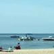 Boats anchored near a beach with people enjoying a sunny day.