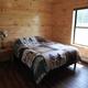 Bedroom interior showing bed, window and wood walls/flooring — useful to represent sleeping accommodations in the cabins.