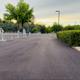 Perspective down a paved driveway/road through the RV park showing hookup stations along the left and hedged perimeter on the right — good orientation shot of park circulation.