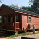 Stand-alone cabin on gravel pad with porch and window AC unit — depicts on-site cabin accommodations (from 'ways to stay' photos on the campground page).