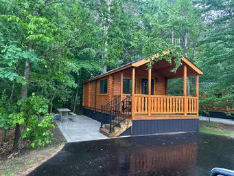 Exterior photo of a standalone cabin with concrete pad, picnic table and surrounding trees — useful for showcasing cabin rentals listed on the property’s cabins page.
