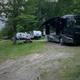 Wide shot of RVs and motorhome parked on gravel/grass pads under trees — good overview of RV sites and typical pitching area (also used as a background image on the site).