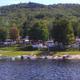 Shoreline view showing a narrow beach with boats and a row of RVs/cabins behind the treeline — clear campsite/park waterfront scene consistent with a lakeside campground on the property's listing page.