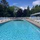 Outdoor swimming pool with clear blue water, white lounge chairs, and trees under a sunny sky