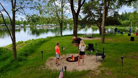 Lakeside tenting/firepit scene with people and grassy shoreline — demonstrates tent sites and lake access, consistent with the site’s tenting/seasonal images.