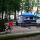 Tent campsite in a wooded area with defined log-bordered pad, chairs and canopy — shows tent camping setup and wooded campsite character on the grounds.