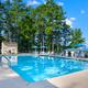 Clear daytime photo of the pool area with chairs, umbrellas and trees — shows an on-site recreational facility. Shown on the resort’s photo gallery page (page: Lake Gaston RV Camping | Thousand Trails RV Campground, URL provided).