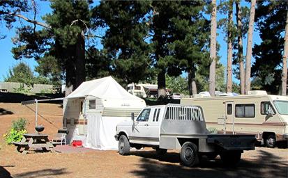 Clear photograph of RVs, tent and campsite area with picnic table and mature trees — directly shows on-site camping facilities. From the Park Rates page (https://www.rervpark.com/rates).