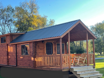 Exterior photo of a family cabin with porch and rocking chairs — good depiction of on-site cabin lodging shown elsewhere on the property pages.