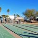 Wide view of outdoor shuffleboard courts with people playing and RVs/landscaping in background — documents on-site recreational amenities visible on the resort page. 