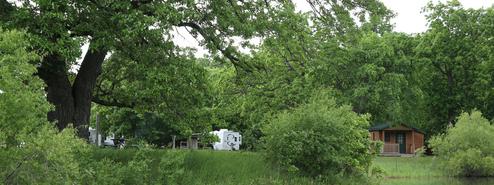 Cleary shows campground amenities: RV, cabin and large shade trees — useful to illustrate lodging/pitch variety and site layout.