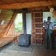 Man at shelves inside wood cabin with black stove and wood bunk