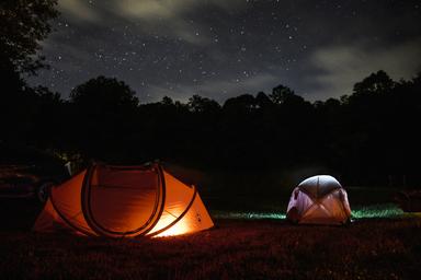 Nighttime tent campsite scene with illuminated tents and stars — useful atmospheric shot highlighting tent camping on the property (used as a homepage/background image).