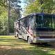 Large RV parked at a campsite with picnic table and trees — shows an on‑site RV pitch with hookups and typical campground layout (from main site gallery).