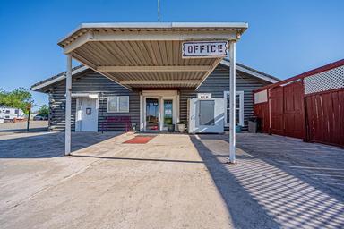 Front-facing image of the office under a canopy showing entrance, paved forecourt and adjacent fencing — good vantage of the main guest check-in area (gallery).