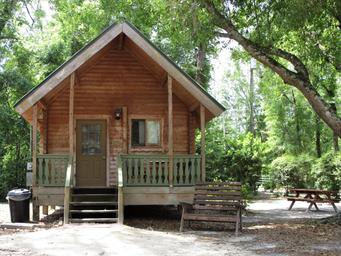 Clear exterior photo of a log cabin on wooded grounds — represents the property's cabin lodging; used as a social/gallery image on the log cabins page.