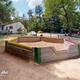 Play area/sandbox and nearby buildings with campground watermark — depicts family recreation area and facilities on the grounds.
