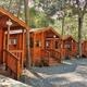 Wide exterior shot showing a row of rustic wooden cabins with gravel paths and picnic tables — clearly depicts the campground’s cabin accommodation and appears on the property homepage banner/background.