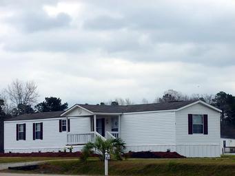 Wide image of a mobile home with landscaped foreground and a lake/trees in the background — good for showing rental unit appearance and grounds (source: Rentals wrapper, rentimages/10.jpg).