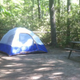 Shaded tent campsite with picnic table in a wooded setting — clear photograph of a campsite on the property (from the site’s main pages showing campground photos).