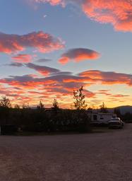 Sunset scene with RVs and parked vehicles silhouetted against colorful sky — demonstrates evening atmosphere and on-site RV spots (homepage/gallery context).