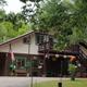 Clear photo of the campground lodge/building with exterior seating, flags and surrounding trees — matches Contact page background and shows an on-site facility.
