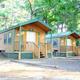 Exterior photo of two deluxe cabins with parking/pads and pine trees — matches the Deluxe Cabin accommodation page and shows typical cabin layout on the property.