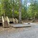 Gravel campsite with raised platform, picnic area and wooden stairs among trees — shows individual campsite layout and amenities on the grounds.