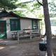 Small cabin with porch, picnic table and lake glimpses beyond — another on-site cabin view that illustrates campsite layout and nearby shoreline (from the resort site).