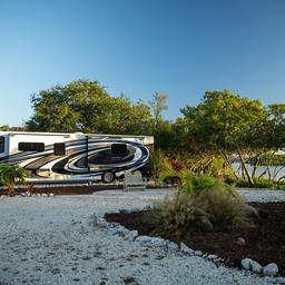 Clear photo of an RV site next to landscaped grounds and water — shows RV pitch layout and on-site vegetation. (waystostay photos).