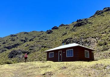 backpacker walks up to cabin at the base of a hill
