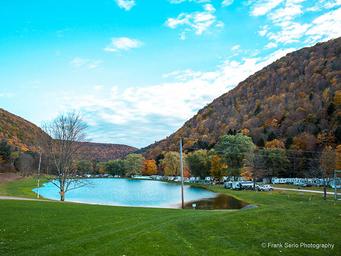 Wide landscape shot of the pond with surrounding campsites and trailers, valley hills in background — good scenic overview used on the campground gallery (Frank Serio photo on site).
