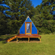 Exterior of a small blue A‑frame cabin on a grassy site with trees behind — clear image of one of the on‑site lodging units featured on the property pages.