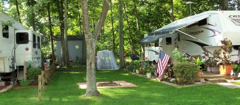 Shows RV sites with level grassy pads, trees, and site details (awnings, decor) — useful to illustrate campsite layout; image is a slide on the campground site.