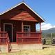 Paddy Flat Guard Station East - front of rustic cabin showing porch and stairs with blue skies and mountains beyond