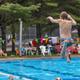 Action shot of a child jumping into the outdoor pool with poolside seating and umbrellas visible — illustrates the on-site pool facility (page: Swim / pool content).