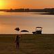 Two children stand near the shore of a lake at sunset
