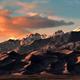 Dramatic shadows play on the sand dunes with tall, snow-covered peaks towering.