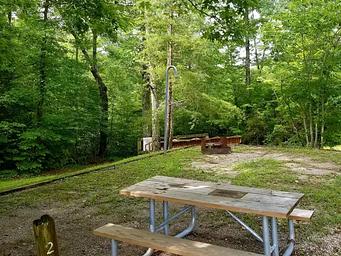 Horse corrals sit near green canopy of forest behind the gravel tent pad of a campsite.