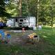 Clear daytime photo of an RV/trailer on a shaded grassy campsite with chairs and a fire ring — shows typical RV site setup on the campground. Source page: homepage (westcanadacreekcampground.com).