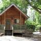 Clear exterior photo of a log cabin on wooded grounds — represents the property's cabin lodging; used as a social/gallery image on the log cabins page.