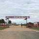 Entrance to Shining Star RV Park with a large sign overhead, American and Texas flags, gravel driveway, trees, buildings, and a person walking.