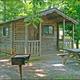 Clear photo of a cabin with picnic table and grill on wooded campground lot — matches cabin accommodations shown on the property website (cabin-2.jpg social image).