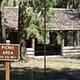 Picnic area sign in foreground,  sunlit group picnic shelter set in conifer forest background.