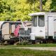 Row of parked RVs on gravel pads with site landscaping and flags — a representative RV campsite view. Photo context on the site shows this as campground RV accommodations.