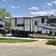 Close-up photograph of a fifth-wheel RV parked on a concrete pad with picnic table and landscaped site — clearly shows an individual RV site at the resort (matches Google-hosted site photo and page context).