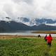Harding River Cabin scenery, four people walking along grassflats to a boat with a river and clod covered mountains in background