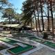 On-ground photo of the mini-golf/course area and clubhouse building near trees and the pond — depicts on-site recreation and facilities.