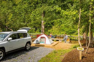 Tent campsite with vehicle parked nearby, tent pad, picnic table and wooded backdrop — depicts tent camping sites on the property (from the campground’s site 'ways to stay' photos).